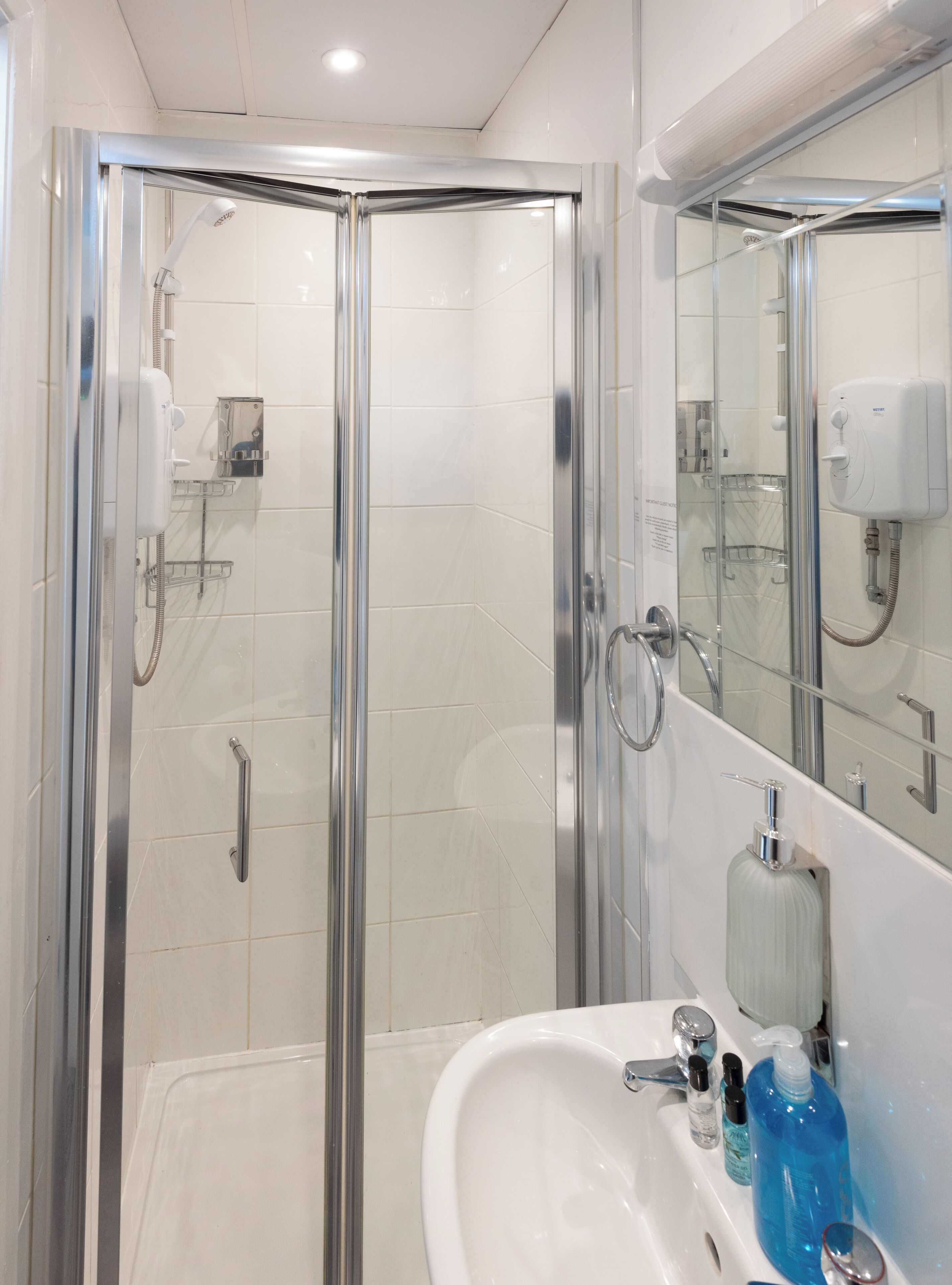 Un baño moderno con ducha de vidrio, un lavamanos blanco con artículos de aseo y un espejo.