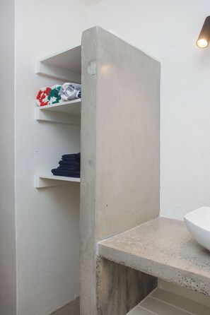 Ein Badezimmer mit einem weißen Waschbecken, einer Beton-Akzentwand und Regalen mit ordentlich gefalteten Handtüchern.