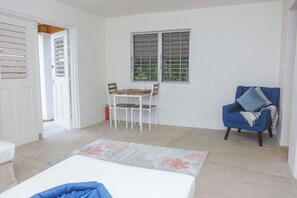 Ein Zimmer mit einem Bett, einem Tisch mit Stühlen, einem blauen Sessel und einem Fenster mit Jalousien.