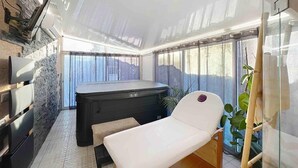 Ett spa-rum med en massagebänk, ett bubbelbad och en vägg av sten.