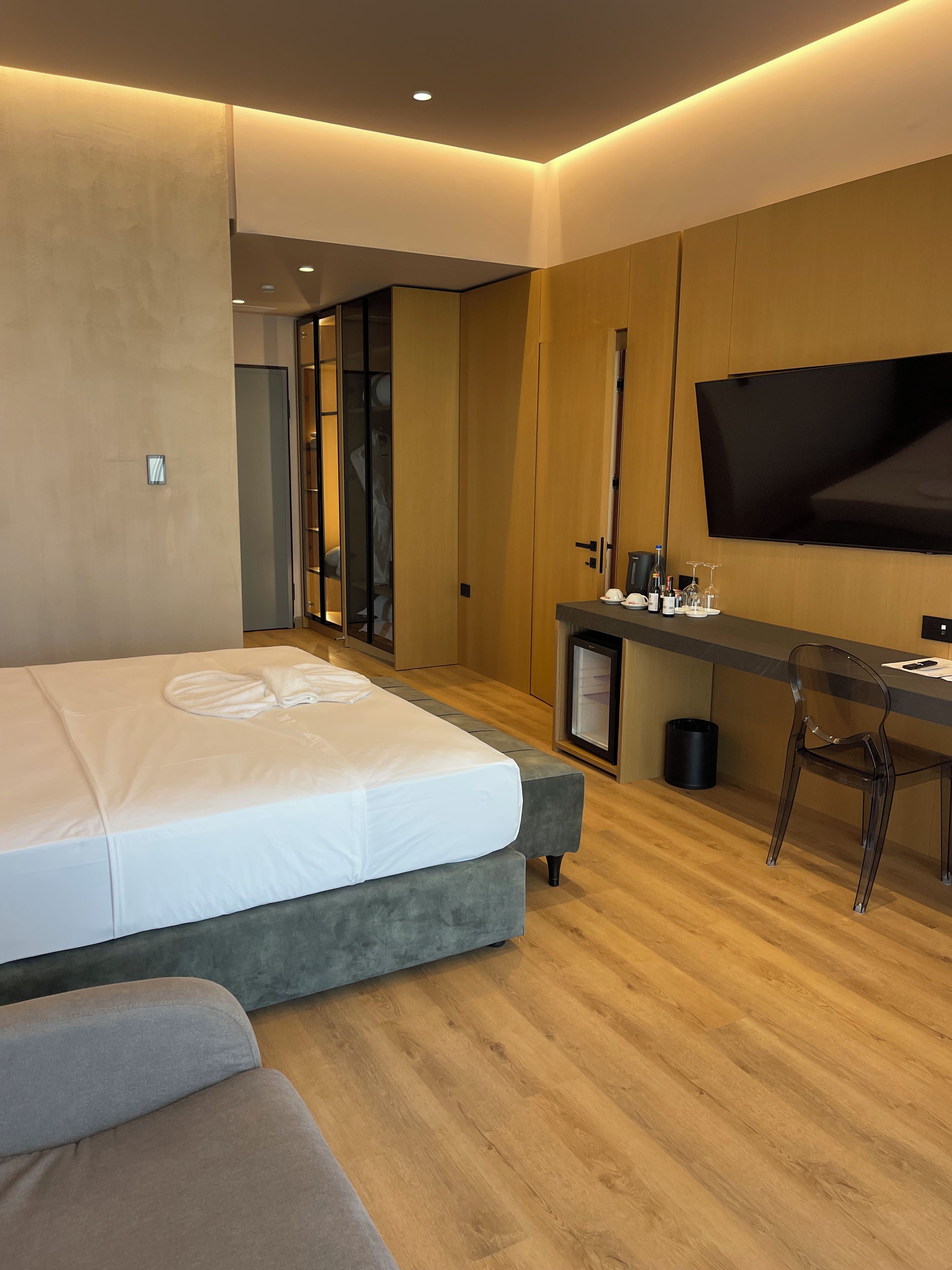 A modern hotel room with a bed, a desk, a chair, a TV, and a minibar.