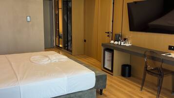 A modern hotel room with a bed, a desk, a chair, a TV, and a minibar.