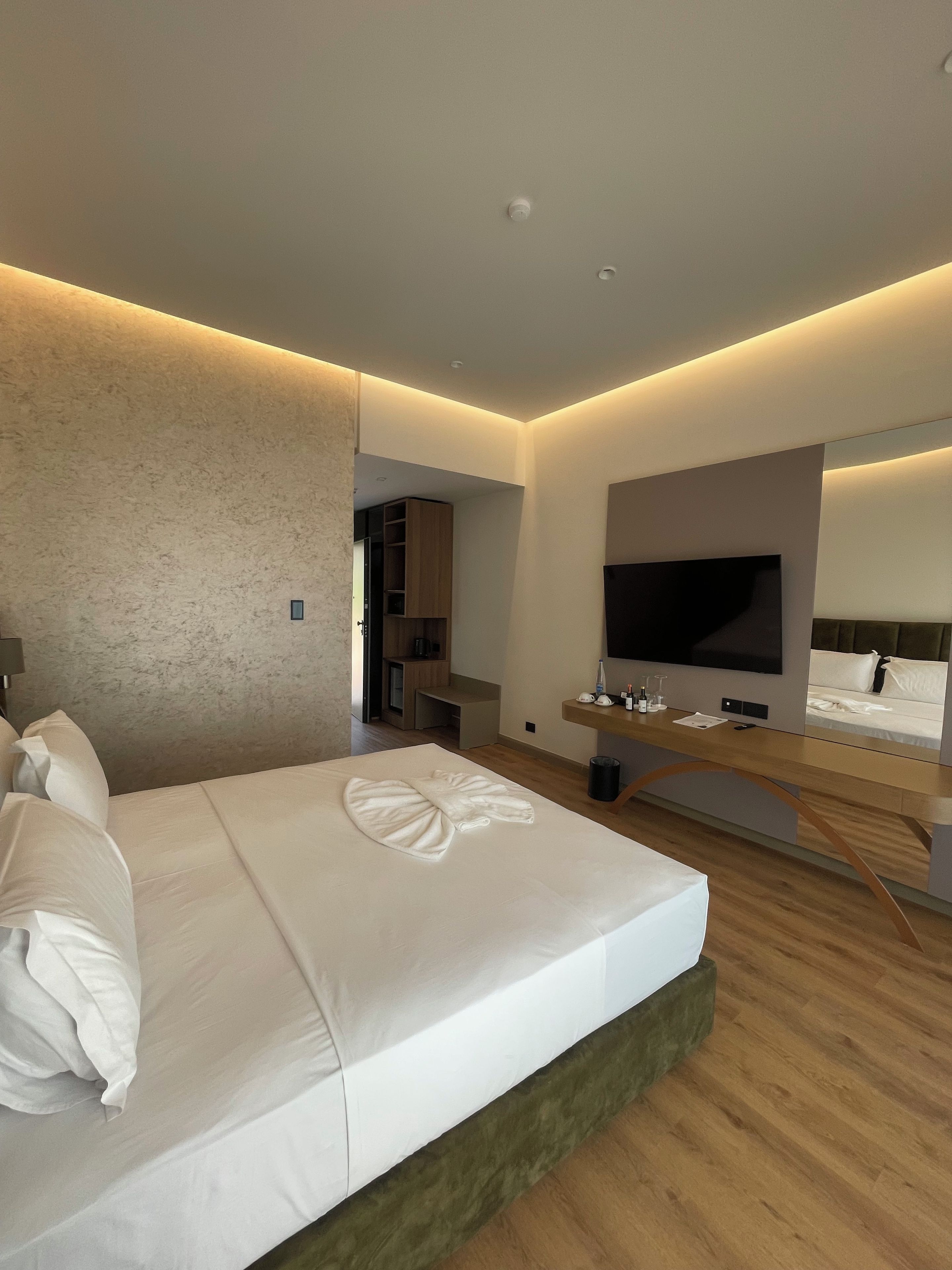 Et moderne hotelværelse med en stor seng, et fladskærms-tv, et skrivebord og et spejl.