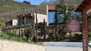 A modern building with a gift shop sign, stone wall, and a view of a hill with trees.