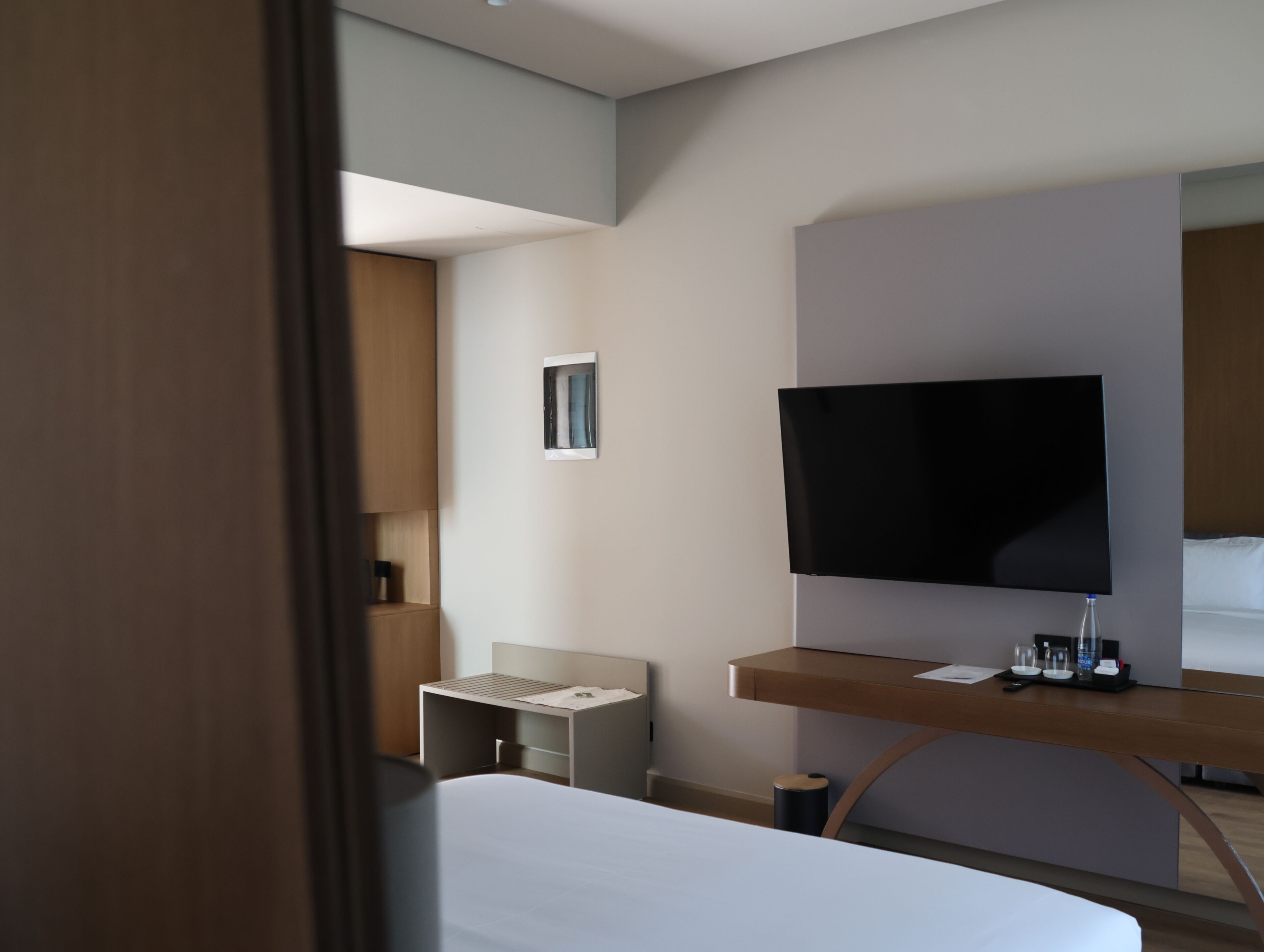 Ein modernes Hotelzimmer mit Bett, Schreibtisch, Flachbildfernseher, kleinem Fenster und Nachttisch.