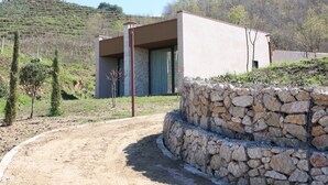 A modern house with a stone wall and a dirt path leading to it.