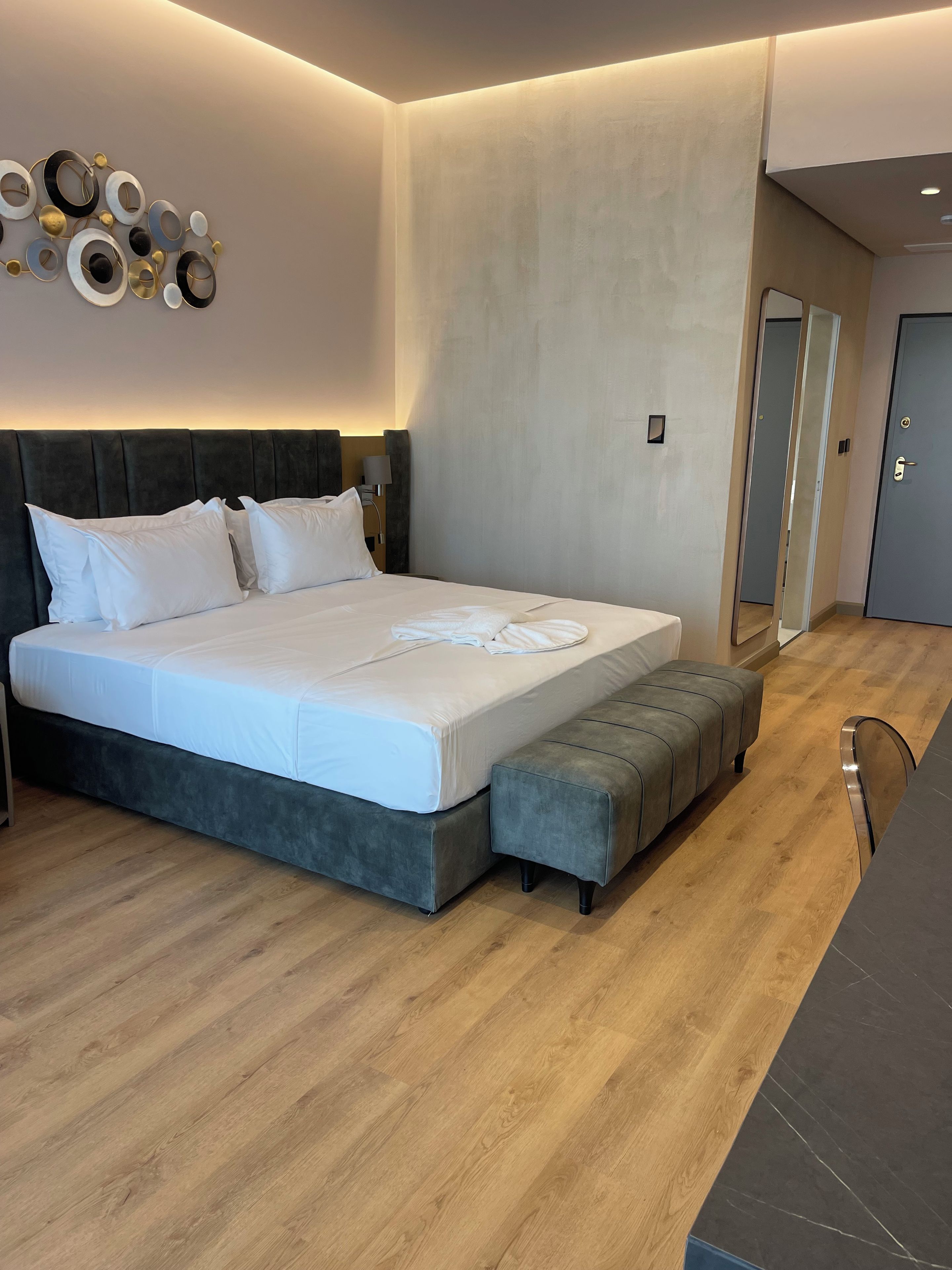 A modern bedroom with a large bed, bedside tables, a bench, and a wall-mounted light fixture.