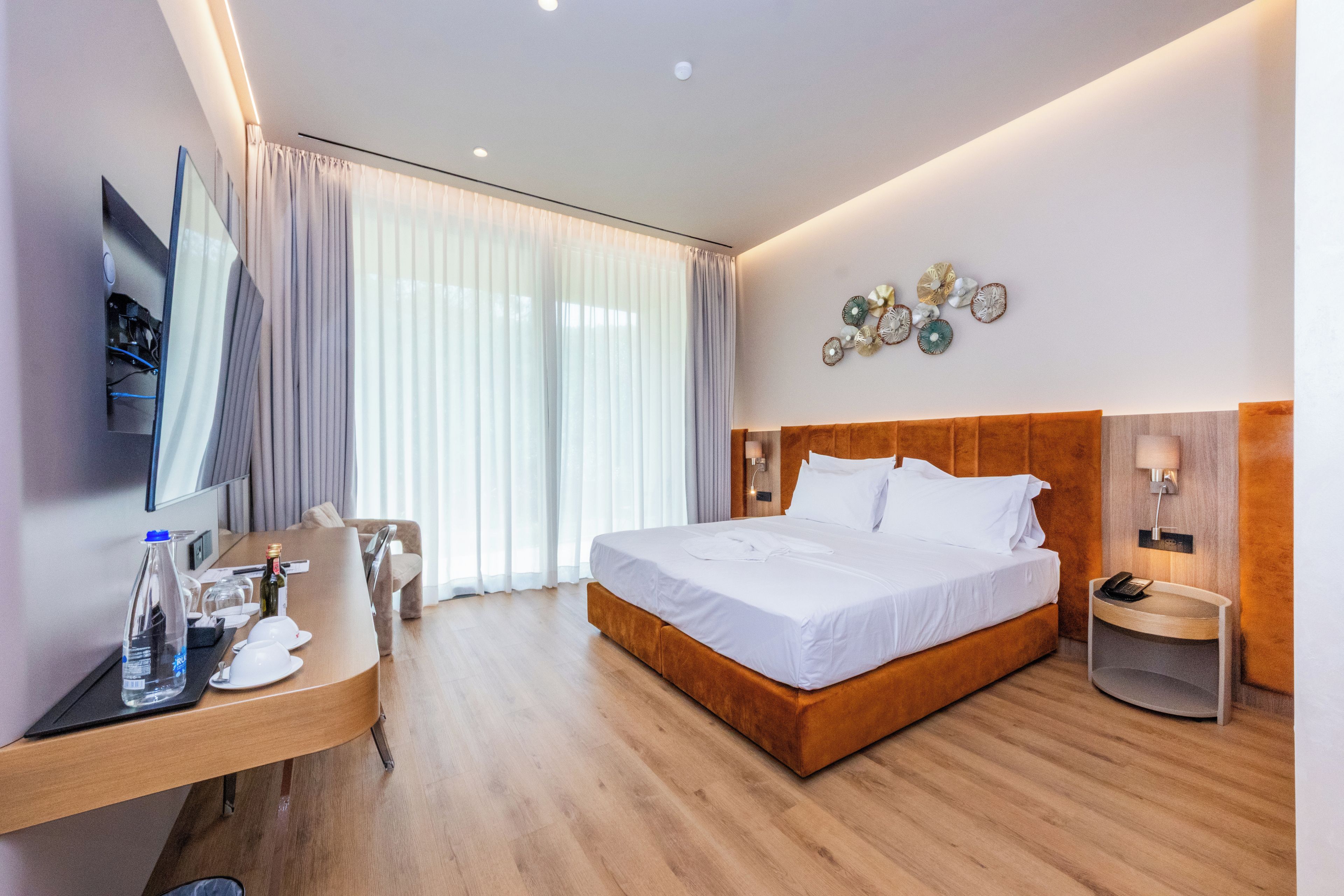 A hotel room with a bed, a desk with a computer, a TV, and a window with curtains.