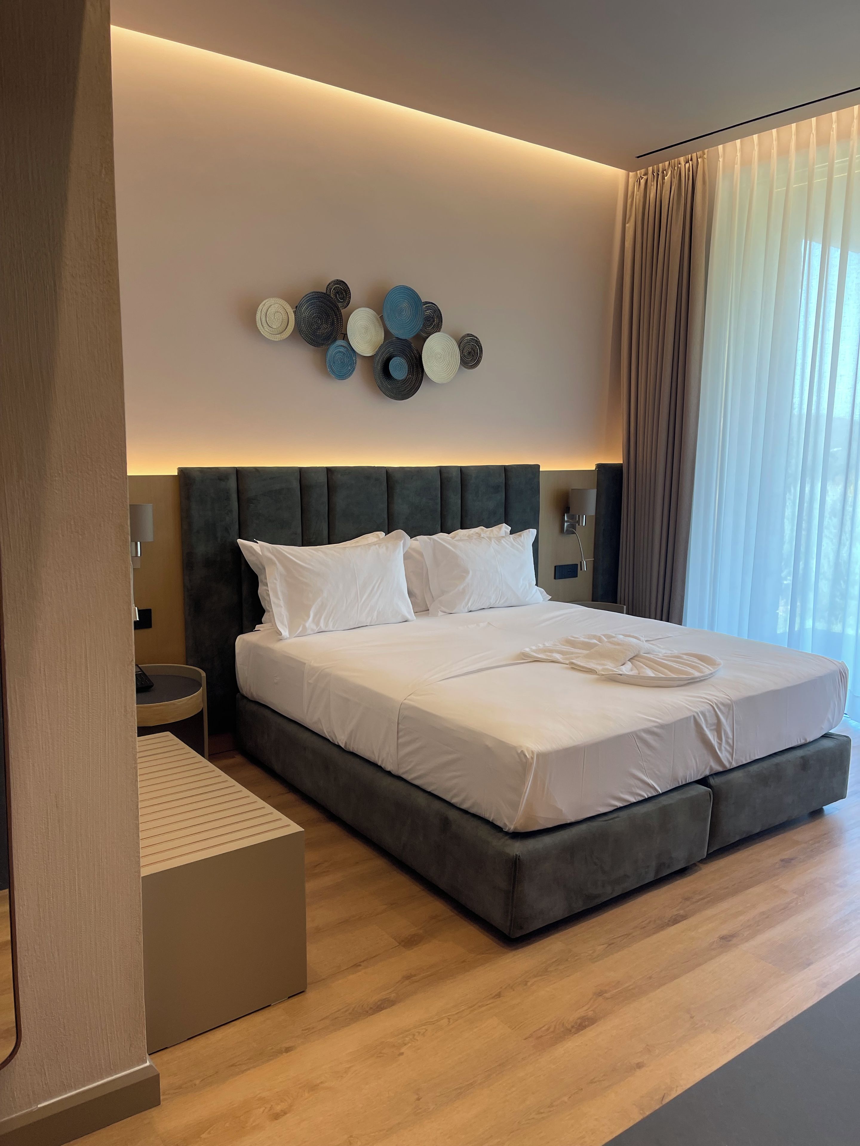 Een moderne hotelkamer met een groot bed, een nachtkastje, een wandlamp en een decoratief kunstwerk aan de muur.