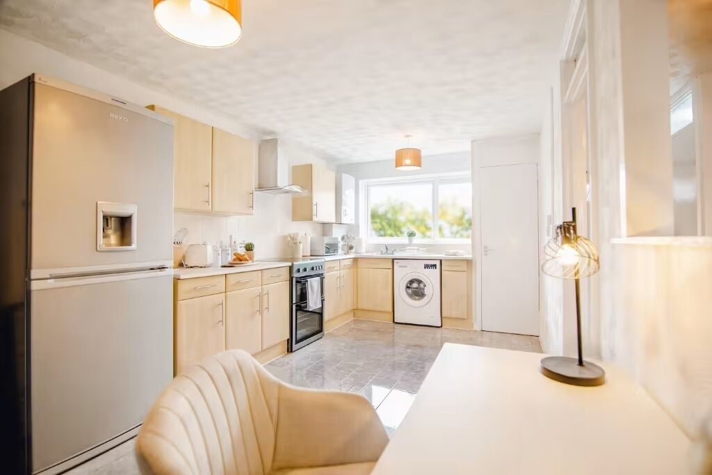 A modern kitchen with a refrigerator, oven, washing machine, and a dining area with a table and chair.
