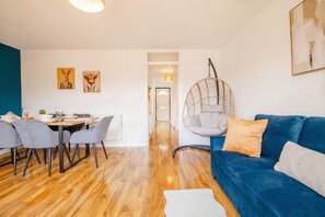 Un saló modern amb un sofà blau, una taula de dinar amb cadires, una cadira penjant i obres d'art a les parets.