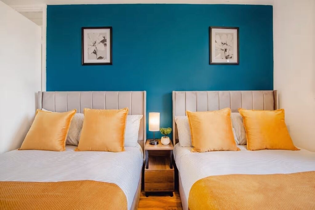 Ein Hotelzimmer mit zwei Betten, einem Nachttisch mit Lampe und zwei gerahmten Bildern an der Wand.