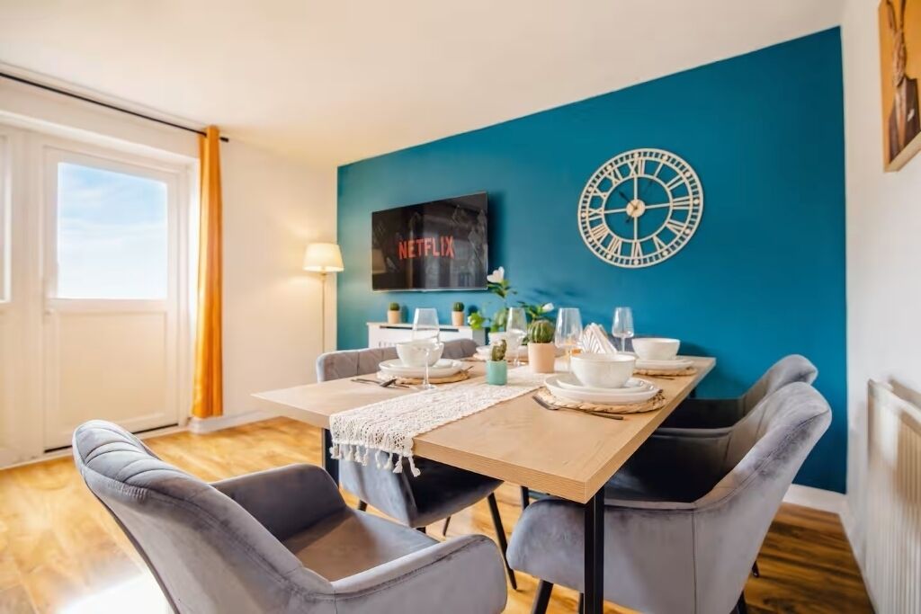 A dining area with a table set for four, a clock on the wall, and a television displaying 'NETFLIX'.