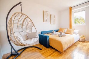 Una habitació amb una cadira penjant, un llit amb capçalera blava i dues obres d'art penjades a la paret.