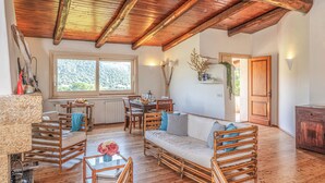 Una habitación con techo de madera, un comedor con mesa y sillas, un sofá y una ventana con vistas a zonas verdes.