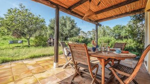 Un patio al aire libre con una mesa y sillas de madera, una pérgola y vistas del follaje circundante.