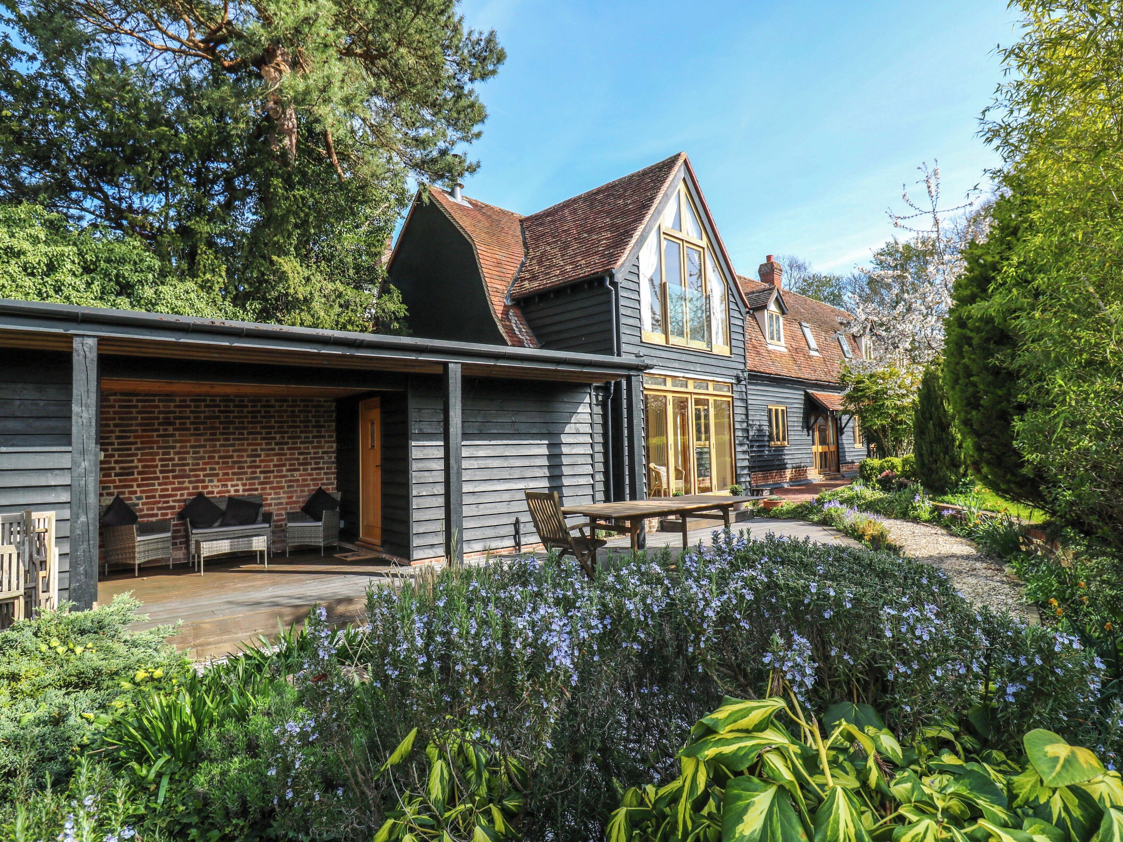 A two-story house with a covered porch, a brick wall, and a garden with various plants and flowers.