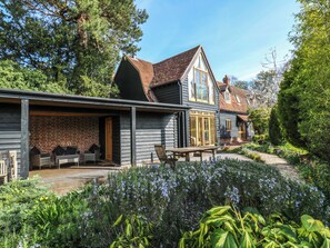 Une maison à deux étages dotée d’un porche abrité, d’un mur en briques et d’un jardin où poussent diverses plantes et fleurs.