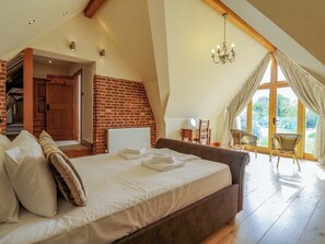 A bedroom with a large bed, a wooden headboard, a brick wall, a chandelier, and a view through large windows. - Six Apples (Braintree)
