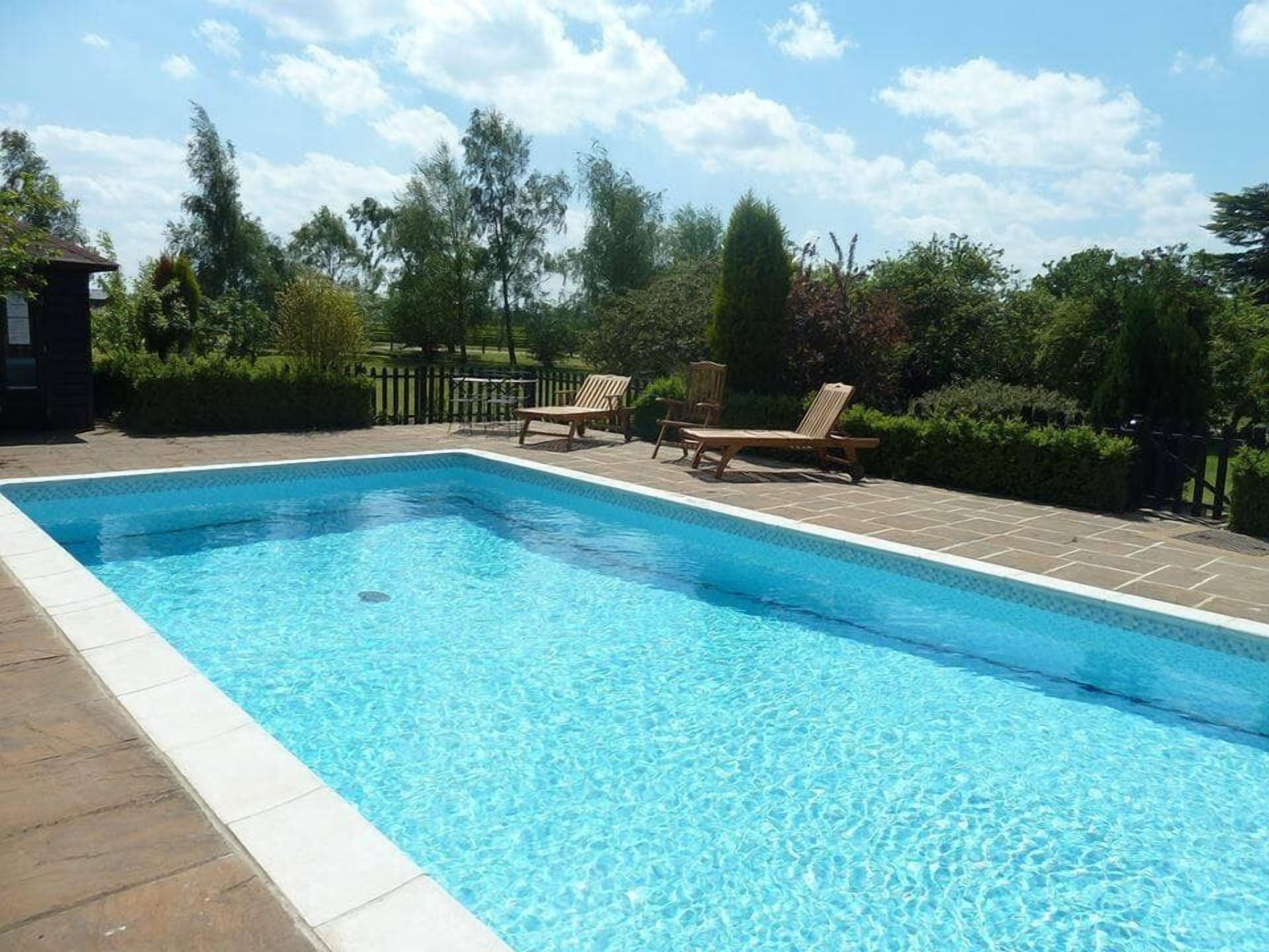 Una piscina rettangolare con acqua cristallina e azzurra, circondata da un solarium piastrellato.