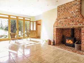 A spacious room with a brick fireplace, large windows, and wicker chairs. - Six Apples (Braintree)
