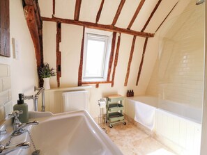 Une salle de bain avec une grande baignoire, une fenêtre, un radiateur et une petite étagère contenant des articles de toilette.