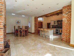 A spacious kitchen with a central island, a dining area with wooden chairs, and a brick wall. - Six Apples (Braintree)