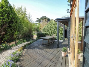 A wooden deck with a table and chairs, surrounded by greenery and a house with a covered patio. - Six Apples (Braintree)