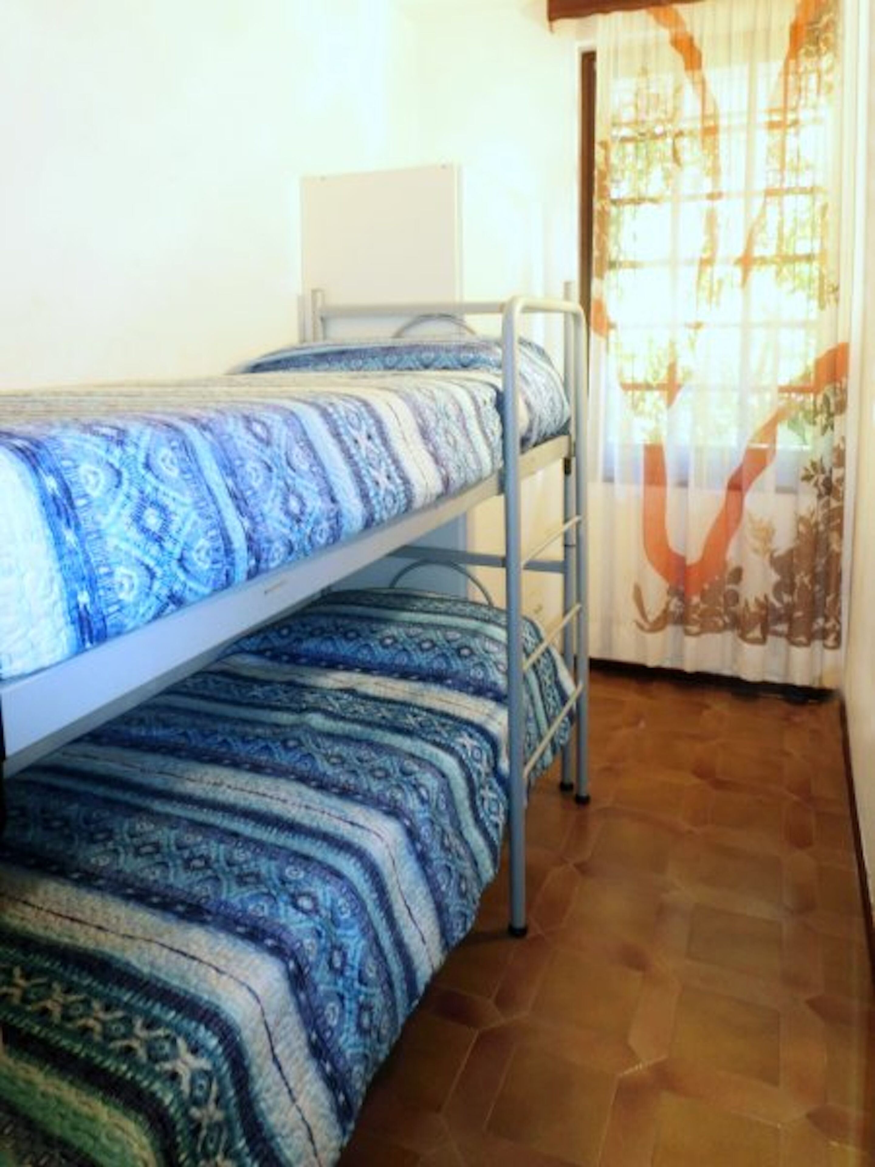 Una cama litera con ropa de cama estampada, una pizarra en la pared y una ventana con cortina.