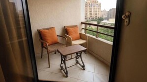 Un balcón con dos sillas y una mesita, vista a edificios y una puerta con cerradura.