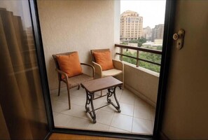 A balcony with two chairs and a small table, a view of buildings, and a door with a lock. - Central Dokki Apartment – Balcony, Metro Access & Great Value (Giza Governorate)
