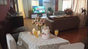 Un comedor con una mesa dispuesta para dos personas, un televisor al fondo y un sofá en la sala.