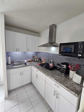 A kitchen with white cabinets, a stainless steel range hood, a microwave, and a tiled backsplash. - Cozy 1-bedroom apartment in pleasant Miami with AC (Miami)