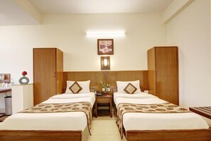 Een hotelkamer met twee bedden, een bureau, een stoel, een nachtkastje, een lamp en een lijst met een foto aan de muur.