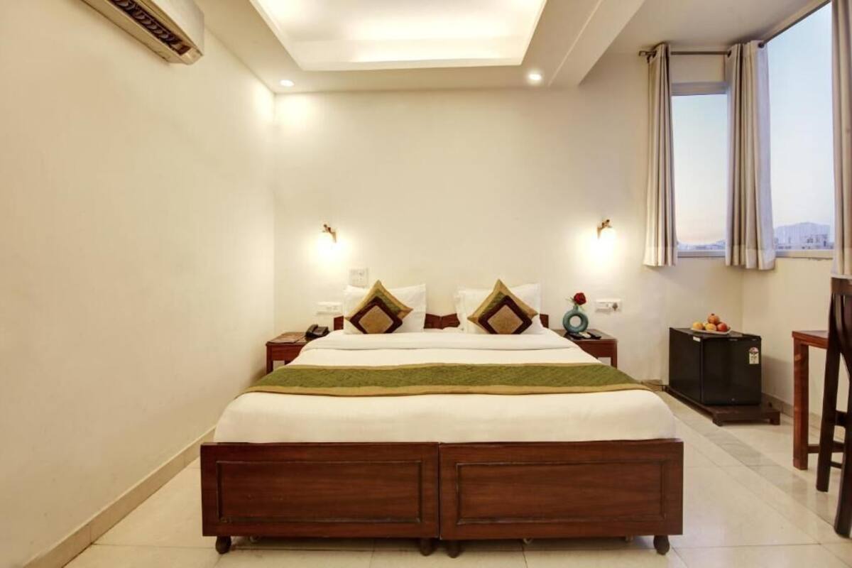 A hotel room with a large bed, bedside tables, a small cabinet, and a window with curtains.