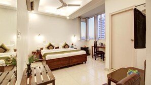 A hotel room with a bed, a desk, a chair, and a ceiling fan. - Marks Hotel (Noida)