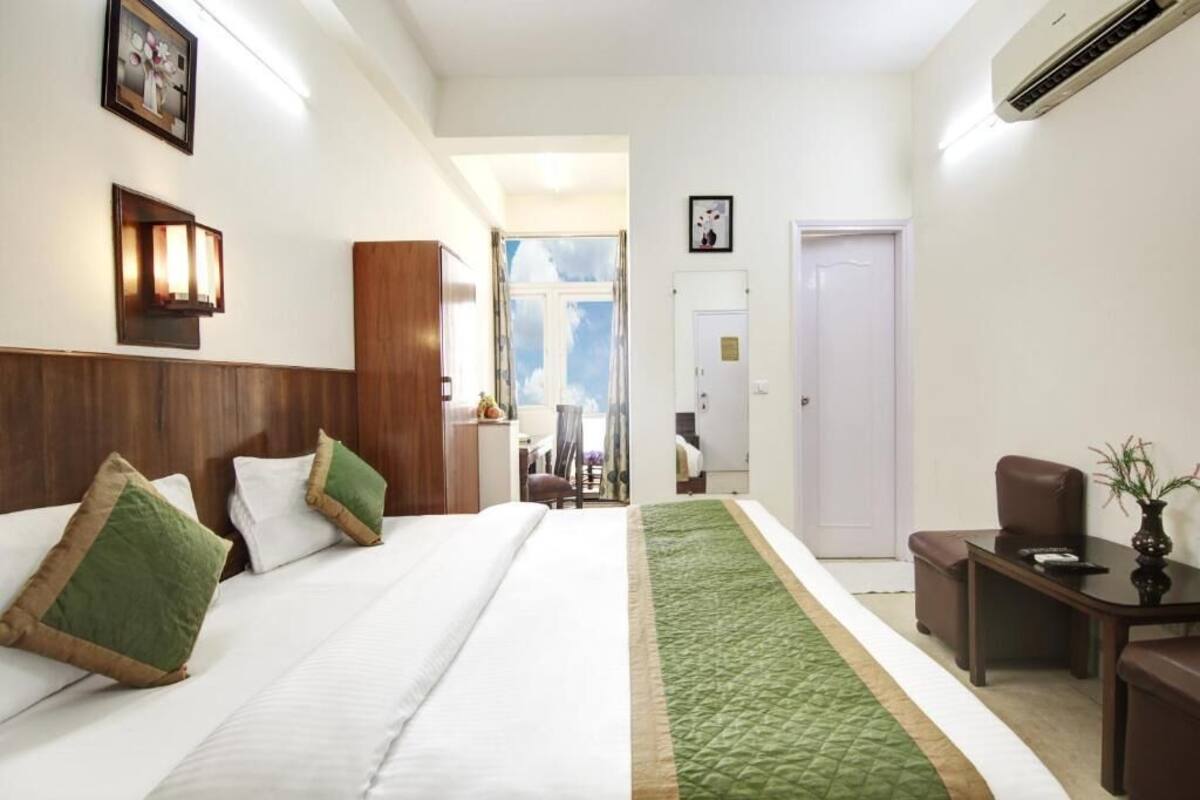 A hotel room with a large bed, a desk, a chair, and a view of the sky through a window.