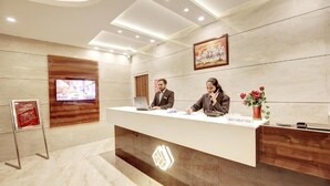 A reception desk with a modern design, a digital display, and a 'May I Help You' sign. - Marks Hotel (Noida)