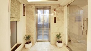 An elevator with marble walls, a potted plant, and a glass shower enclosure. - Marks Hotel (Noida)