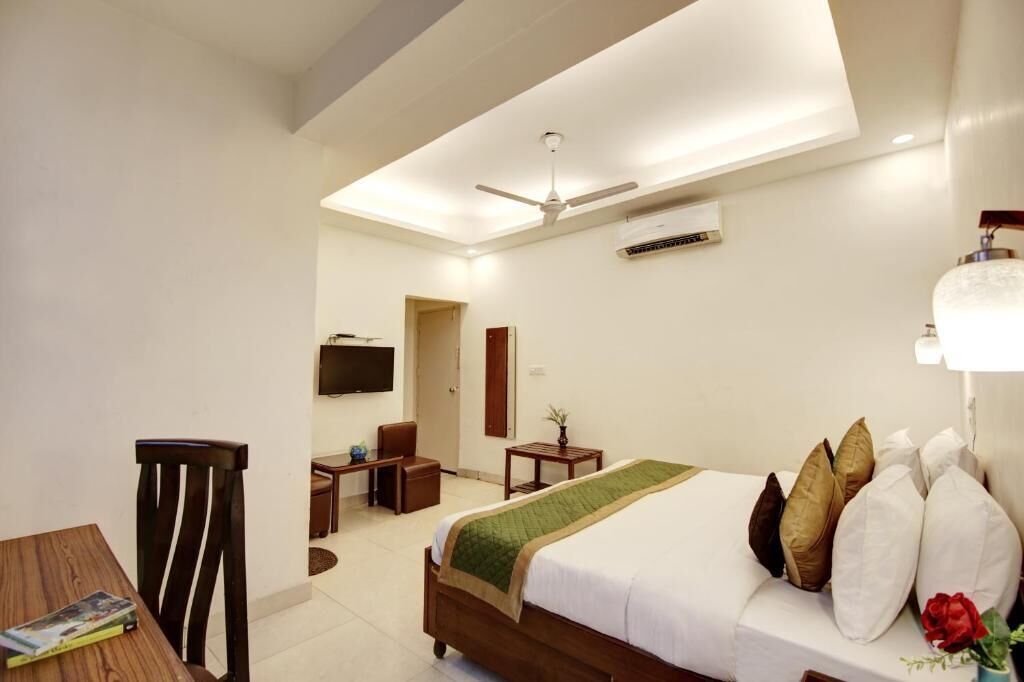 A hotel room with a bed, a desk, a chair, a television, and a ceiling fan.
