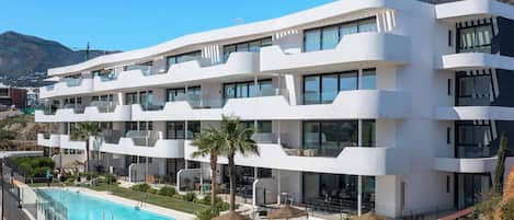 A multi-story hotel with a swimming pool, outdoor seating, and a view of the surrounding landscape.