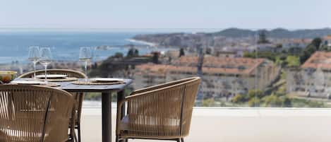 A dining area with wicker chairs and a table, overlooking a coastal cityscape.