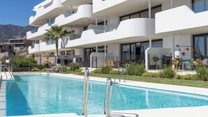 A modern hotel with a swimming pool, outdoor seating, and a view of the mountains. - Luxury 3-Bedroom Skyline Apartment in Higueron (Fuengirola)