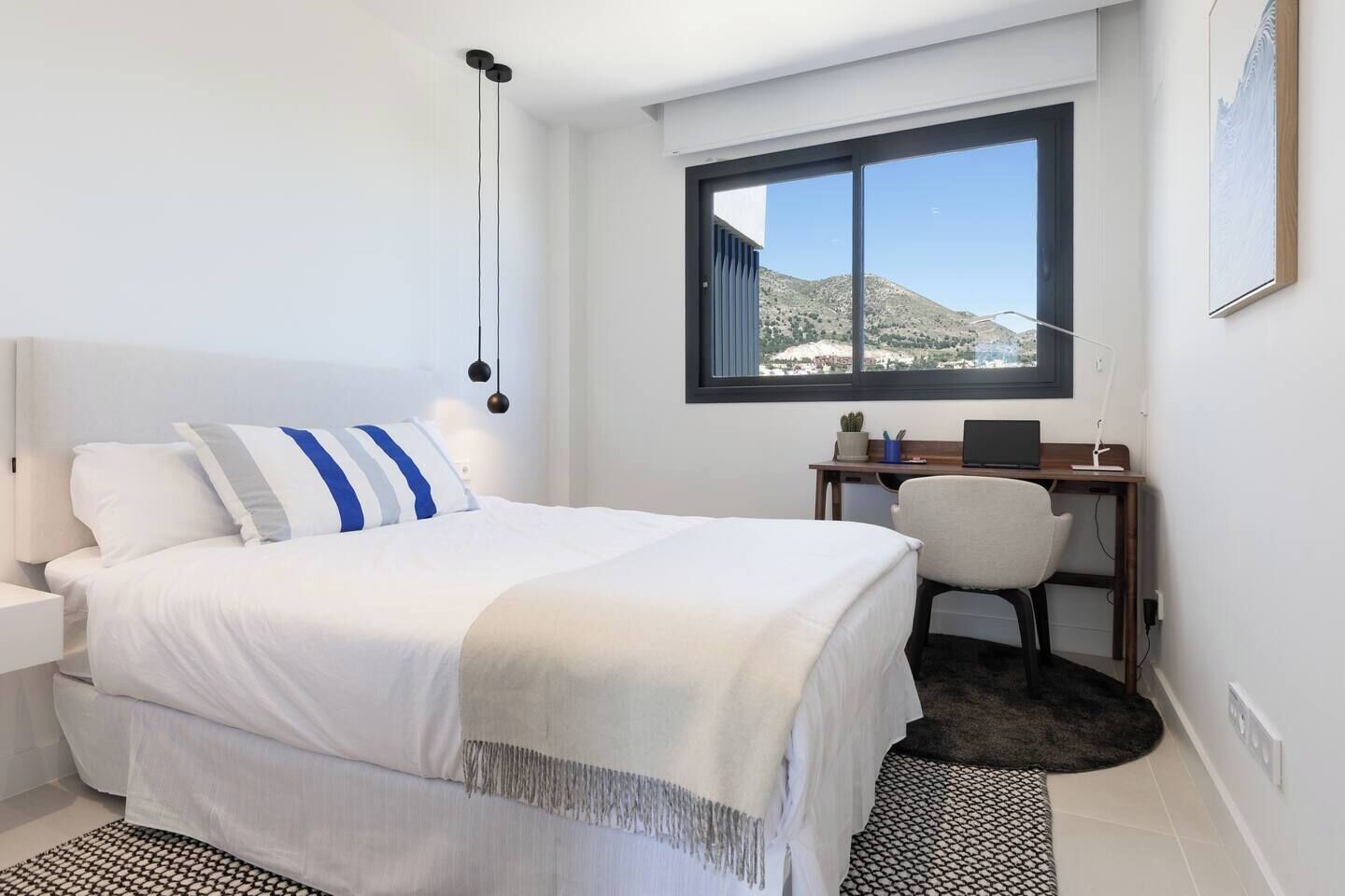 Quarto moderno com cama, escrivaninha e vista para uma montanha.
