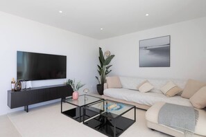 Een moderne woonkamer met een flatscreen televisie, een glazen salontafel, een bank en een grote potplant.