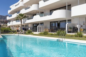 A modern hotel with a swimming pool, multiple balconies, and a view of the mountains. - Luxury 3-Bedroom Skyline Apartment in Higueron (Fuengirola)