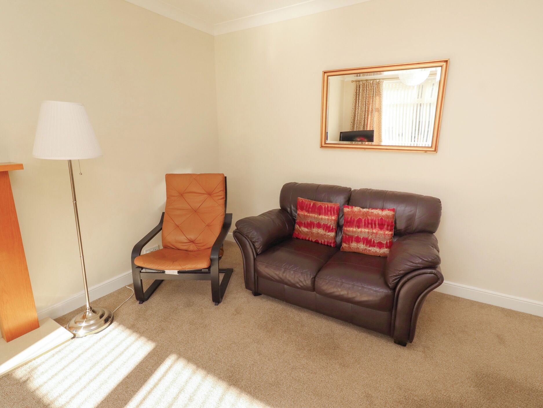 A living room with a brown leather sofa, a matching armchair, a floor lamp, and a mirror on the wall.