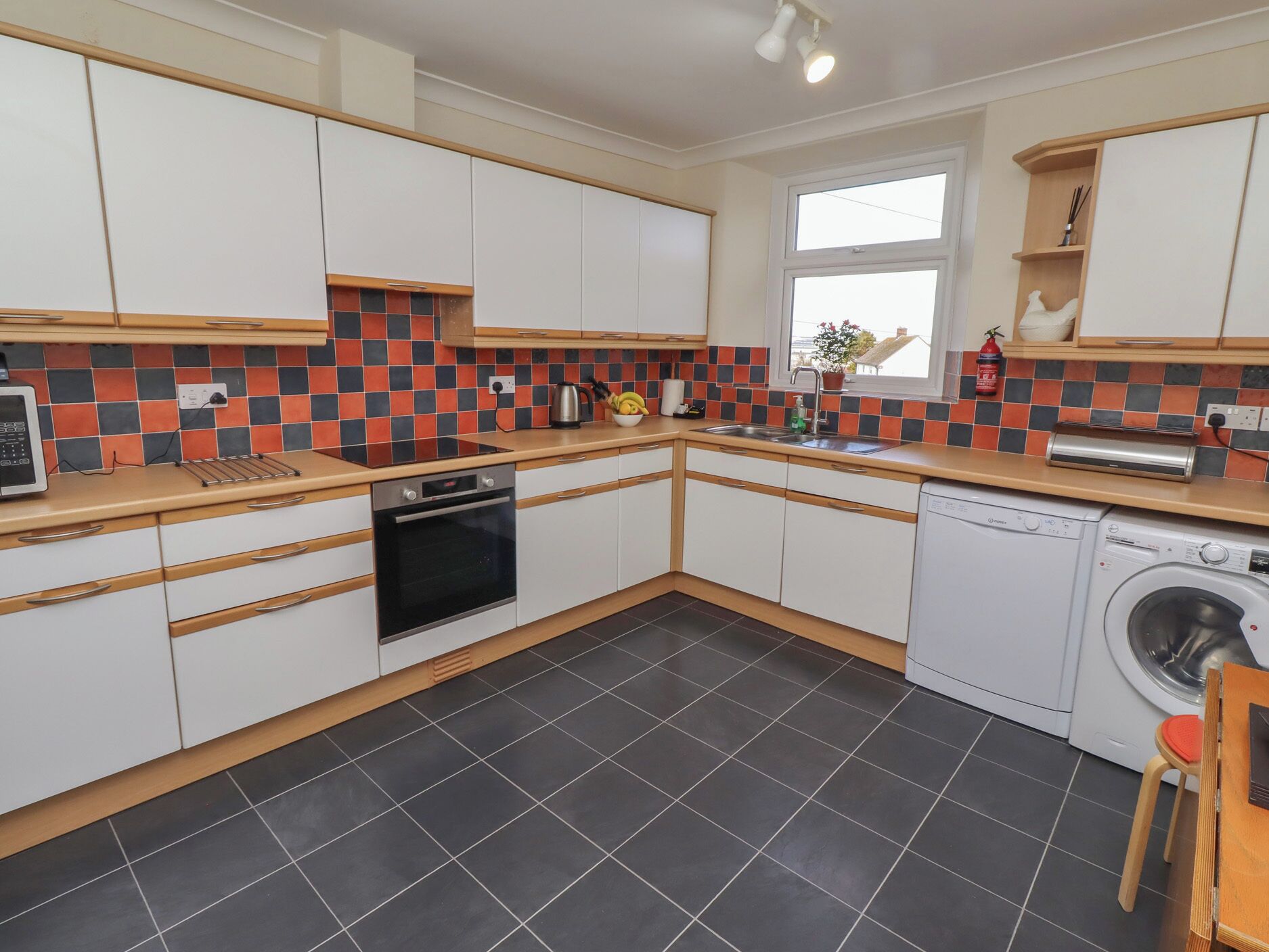 Et moderne køkken med hvide skabe, en sort ovn, en vaskemaskine og et flisebeklædt backsplash.