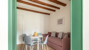 Een kamer met een houten plafond, een ronde tafel met stoelen, een bank met kussens en een ingelijst schilderij aan de muur.