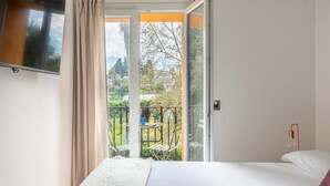 Een slaapkamer met een bed, een aan de muur bevestigde televisie, een balkon met een tafel en stoelen, en een airconditioning.
